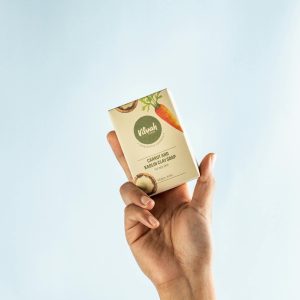 A close-up of a hand holding a natural handmade soap bar against a light background.