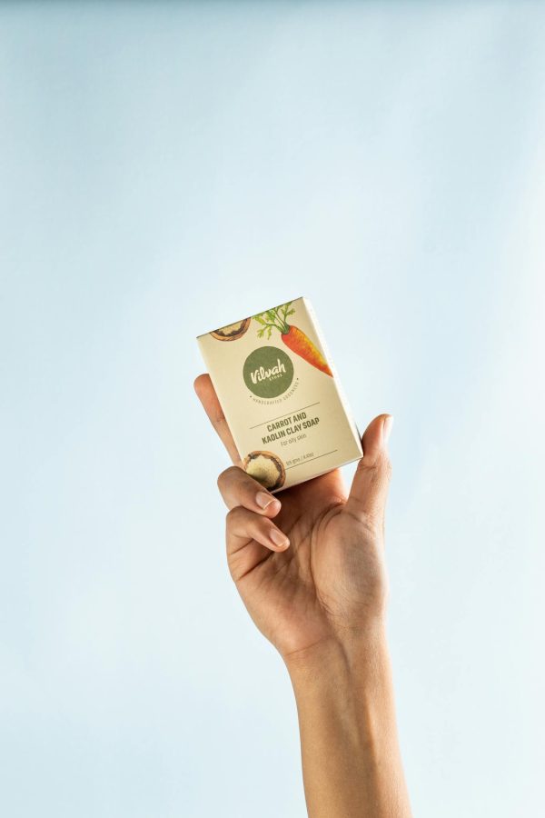 A close-up of a hand holding a natural handmade soap bar against a light background.