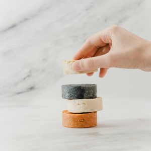 A hand arranging a stack of eco-friendly natural soap bars on a marble surface.