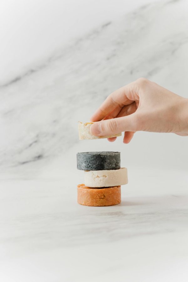 A hand arranging a stack of eco-friendly natural soap bars on a marble surface.