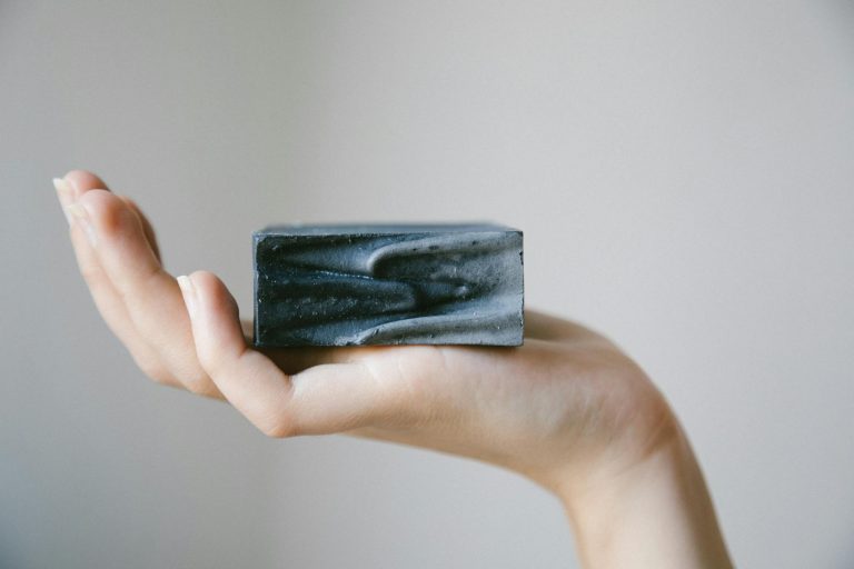 A minimalist image of a hand holding a charcoal soap bar, showcasing clean beauty concepts.