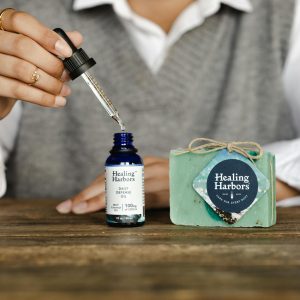 Close-up of Healing Harbors CBD oil and soap set on wooden table, with hand using dropper.