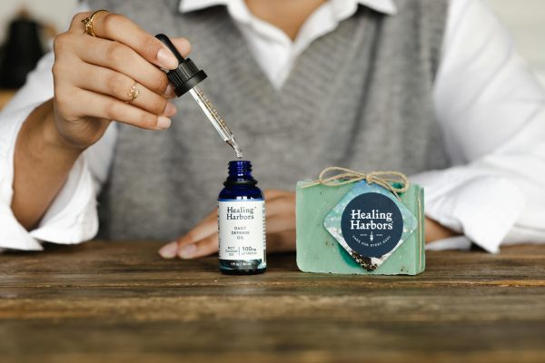 Close-up of Healing Harbors CBD oil and soap set on wooden table, with hand using dropper.