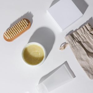 Flat lay of skincare products including a brush, container, and pouch on a white surface.