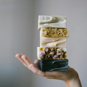 Stack of colorful handmade soaps with floral details displayed on a hand, showcasing artisanal craftsmanship.