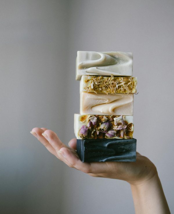 Stack of colorful handmade soaps with floral details displayed on a hand, showcasing artisanal craftsmanship.